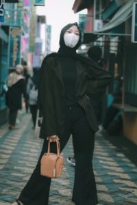 woman in black coat and white mask holding brown leather handbag
