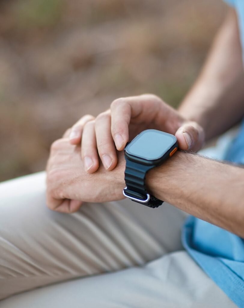 A man adjusts his smartwatch while sitting outdoors, emphasizing modern technology use.